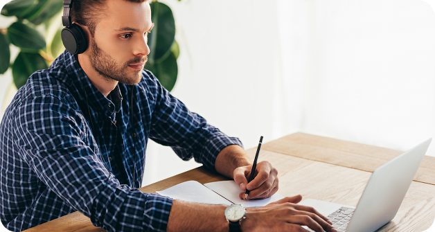 Man with headphones taking notes from laptop