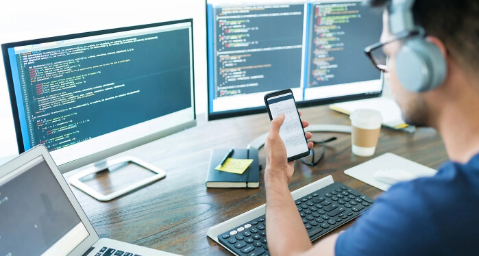 Man viewing code on mobile with computer behind
