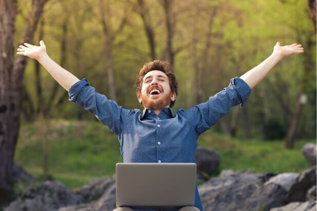 Happy man with laptop stretching in nature