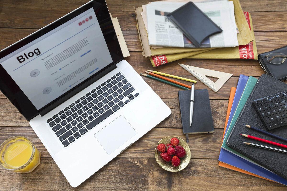Laptop showing blog on desk covered with paper and snacks