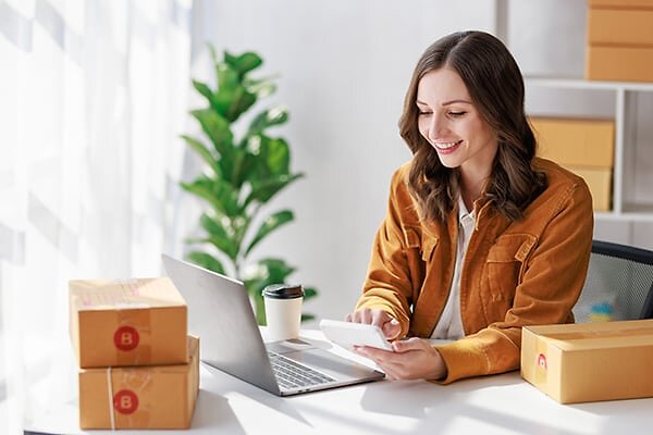 Woman with packing boxes smiling at phone in hand