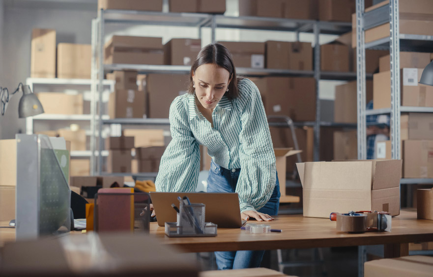 Woman Surrounded By Packaging Boxes Viewing Laptop